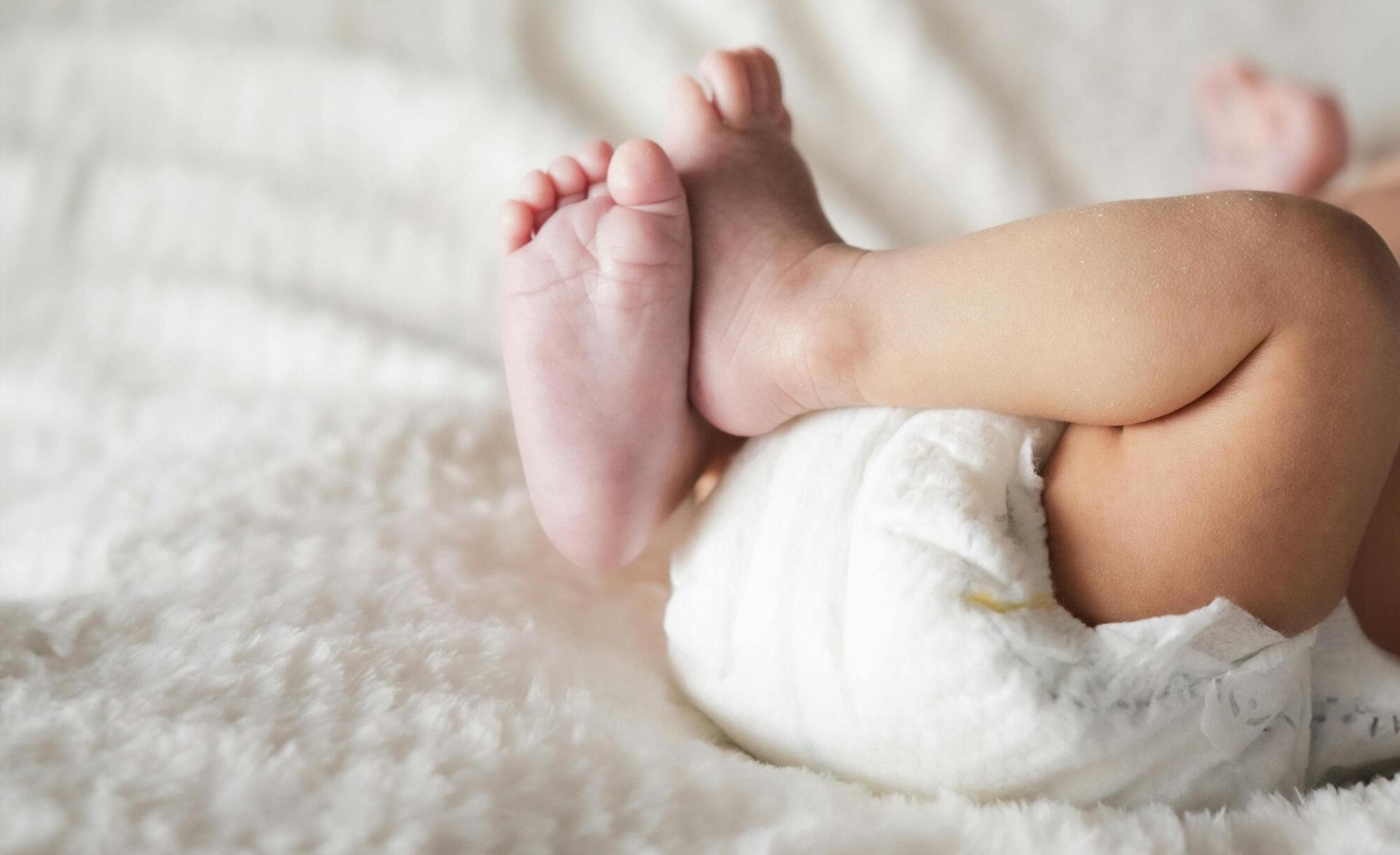Bebé deitado com fralda branca, pernas e pés visíveis em fundo claro
