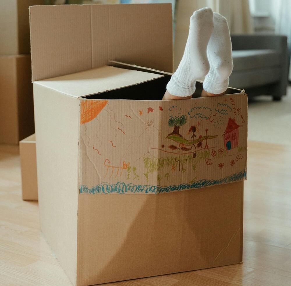 Caixa de cartão decorada com desenhos coloridos e pés de criança com meias brancas para cima