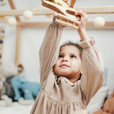 Criança com vestido bege segura brinquedo de madeira avião no quarto decorado