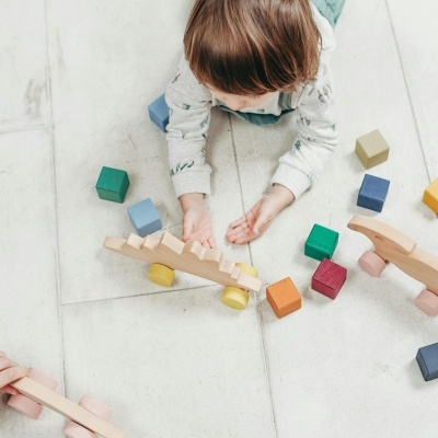 Criança deitada no chão a brincar com brinquedos de madeira coloridos
