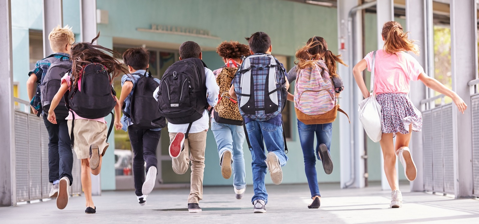 Crianças a correr com mochilas em corredor ao ar livre