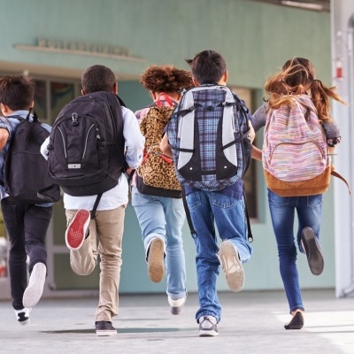 Crianças a correr com mochilas em corredor ao ar livre