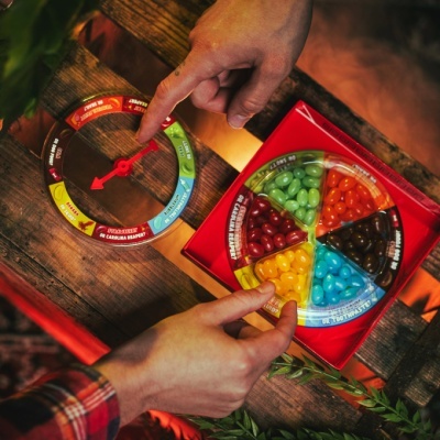 Jogo de tabuleiro com gomas de várias cores e botão giratório vermelho sobre mesa de madeira