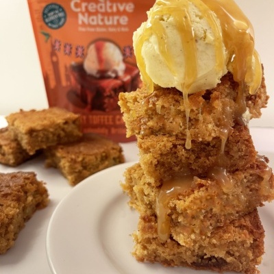 Barras de bolo empilhadas com gelado e molho, embalagem Creative Nature ao fundo.