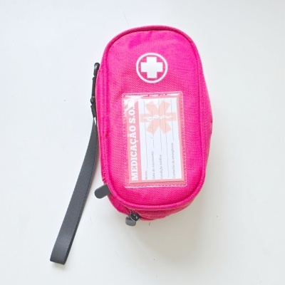 Bolsa de primeiros socorros rosa com cruz branca e etiqueta MEDICAÇÃO S.O.S.