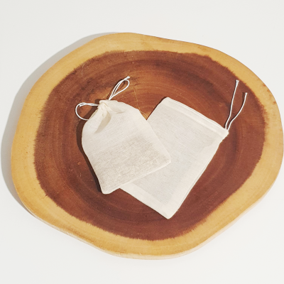 Duas bolsas pequenas de tecido branco com cordões, sobre madeira natural