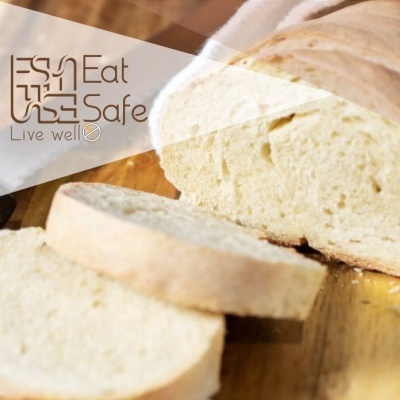 Pão branco fatiado sobre superfície de madeira com texto 'Eat Safe Live well'.