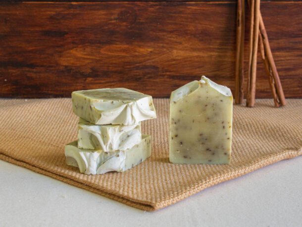 Sabão artesanal de de Alecrim Ginkgo e Urtiga - Miristica Sabonetes verdes claros com manchas escuras em superfície bege e fundo de madeira