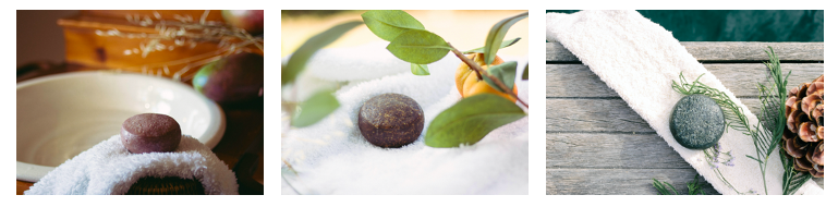 Sabonetes esfoliantes redondos castanho, verde e cinzento sobre sal grosso e toalhas brancas com elementos naturais.