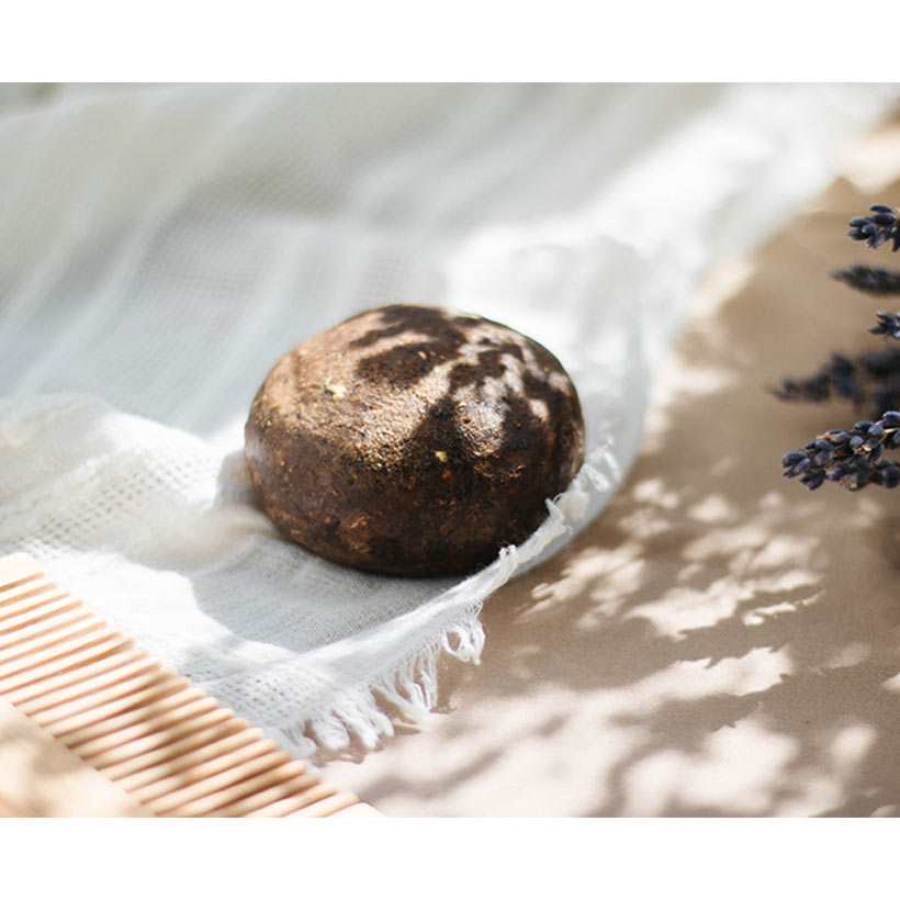 Sapone tondo marrone con macchie su tessuto bianco e pettine di legno