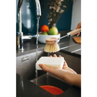 Escova de lavar louça com cabo de madeira e cerdas claras junto a barra de sabão branca em pia de cozinha