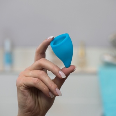Mão segurando copo menstrual azul de silicone