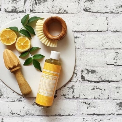 Produtos de limpeza naturais em superfície de azulejos brancos, incluindo sabão de castela, escova, rolo de limão e limões cortados.