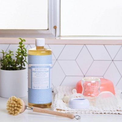 Utensílios de limpeza e plantas em bancada de cozinha branca com azulejos geométricos.