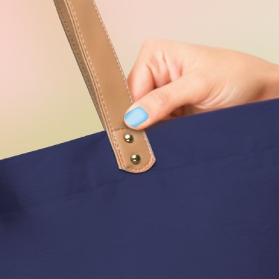 Mão segurando alça de pele bege com rebites num tecido azul escuro.