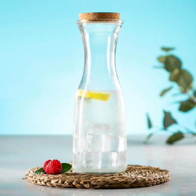 Garrafão de vidro com água, gelo e limão sobre descanso de palha com framboesa e folha