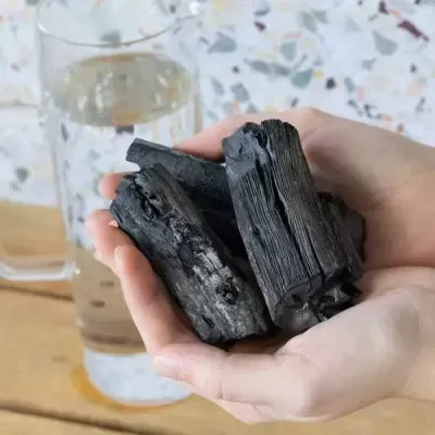 Mãos segurando carvão vegetal perante um copo de água