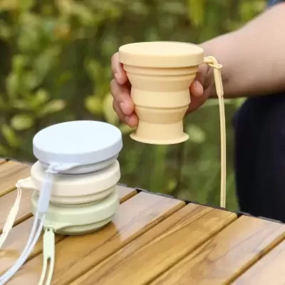 Garrafa dobrável em silicone de cores pastel em mesa de madeira ao ar livre