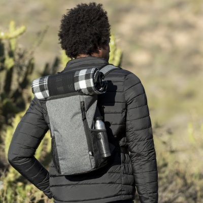 Mochila cinzenta com manta quadriculada na parte superior usada por pessoa com casaco preto em ambiente exterior