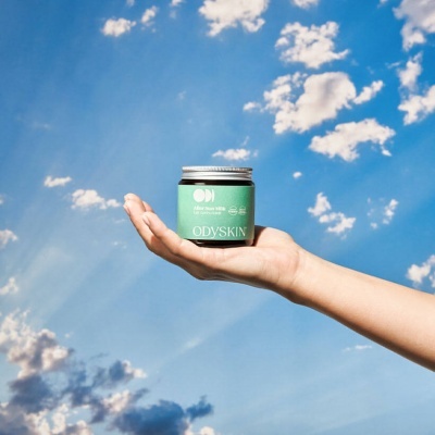 Frasco verde de cosmético ODYSKIN contra céu azul com nuvens