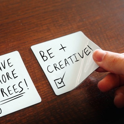 Dois cartões brancos com mensagens manuscritas, um a ser segurado por uma mão sobre uma mesa de madeira.