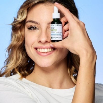 Mulher sorridente segurando frasco de ácido hialurônico com rótulo azul e branco