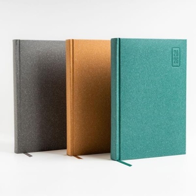 Três agendas coloridas com capas texturizadas e inscrição 2026 na capa verde-azulada