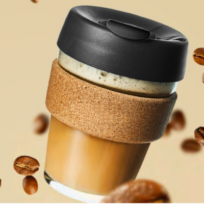 Copo reutilizável para café com tampa preta e faixa de cortiça rodeado por grãos de café