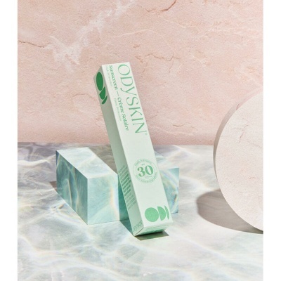 Caixa de produto cosmético ODYSKIN com proteção solar SPF 30 sobre bloco marmoreado e fundo rosa