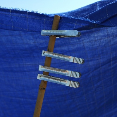 Quatro prendedores de roupa metálicos enferrujados presos num pau de madeira em tecido azul