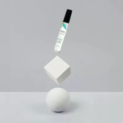 Frasco de vidro transparente com tampa preta e rótulo LEGERE, sobre cubo branco em esfera branca