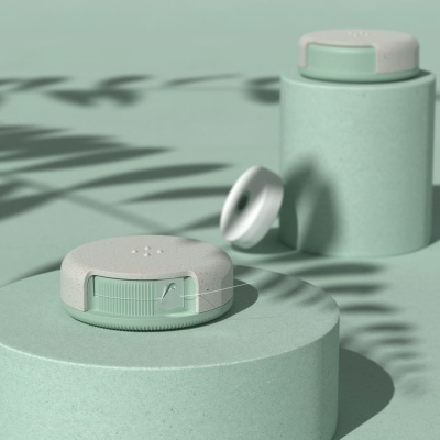 Frascos verdes foscos com acabamento redondo e tampa aberta em ambiente com sombras de folhas.