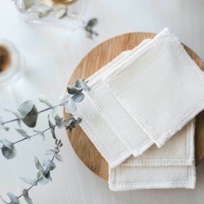 Toalhetes brancos de tecido num prato de madeira com ramo de folhas ao lado
