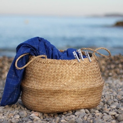Cesto de palha com tecido azul em praia de pedras perto do mar