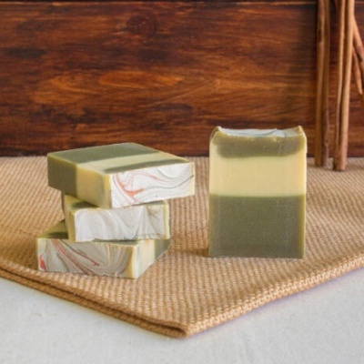 Sabonetes artesanais verde e creme com padrão marmoreado sobre esteira bege e fundo madeira.