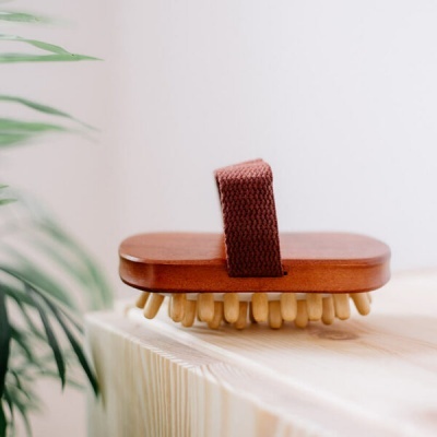 Escova de madeira com alça de tecido castanho numa superfície de madeira clara.