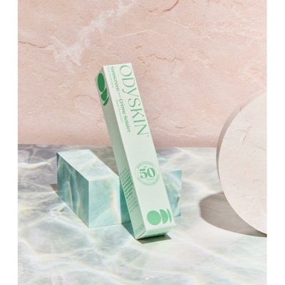 Embalagem de creme solar ODYSKIN FPS 50 em fundo rosa claro e superfície translúcida