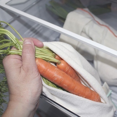 Mão a segurar cenouras num saco de tecido dentro de um frigorífico