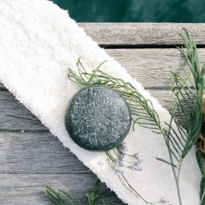 Pedra redonda cinzenta sobre toalha branca com ramos verdes e pinha em madeira