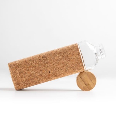 Garrafa de vidro com capa de cortiça e tampa de madeira inclinada sobre uma superfície branca