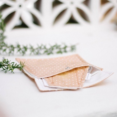 Máscaras de tecido bege com pontos brancos sobre mesa branca e ramos verdes ao fundo