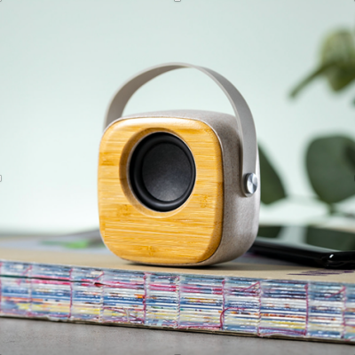 Coluna de som portátil em betão e madeira sobre livros coloridos num ambiente interior com plantas
