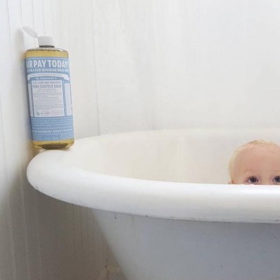 Frasco de spray azul e amarelo na borda de uma banheira branca com criança atrás.