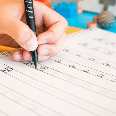 Mão escrevendo letras cursivas com caneta preta em papel pautado