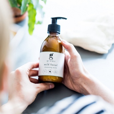 Frasco de cleansing milk facial com doseador segurado por mãos.