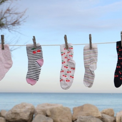 Cinco pares de meias coloridas penduradas num estendal ao ar livre junto ao mar