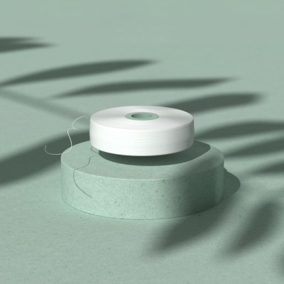 Rolo de fio branco sobre base verde clara com sombras de folhas