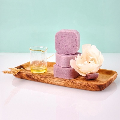Sabonetes cor de rosa empilhados em travessa de madeira com copo de vidro e flor branca