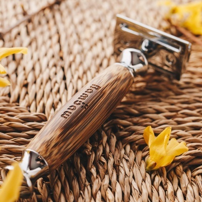 Aparelho de barbear com cabo de madeira e metal sobre superfície trançada com pétalas amarelas