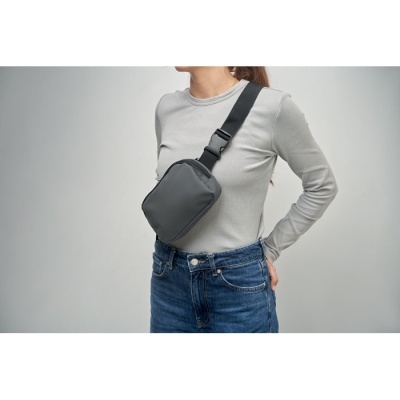 Mulher com t-shirt cinzenta e jeans azuis usando mala preta cruzada no peito